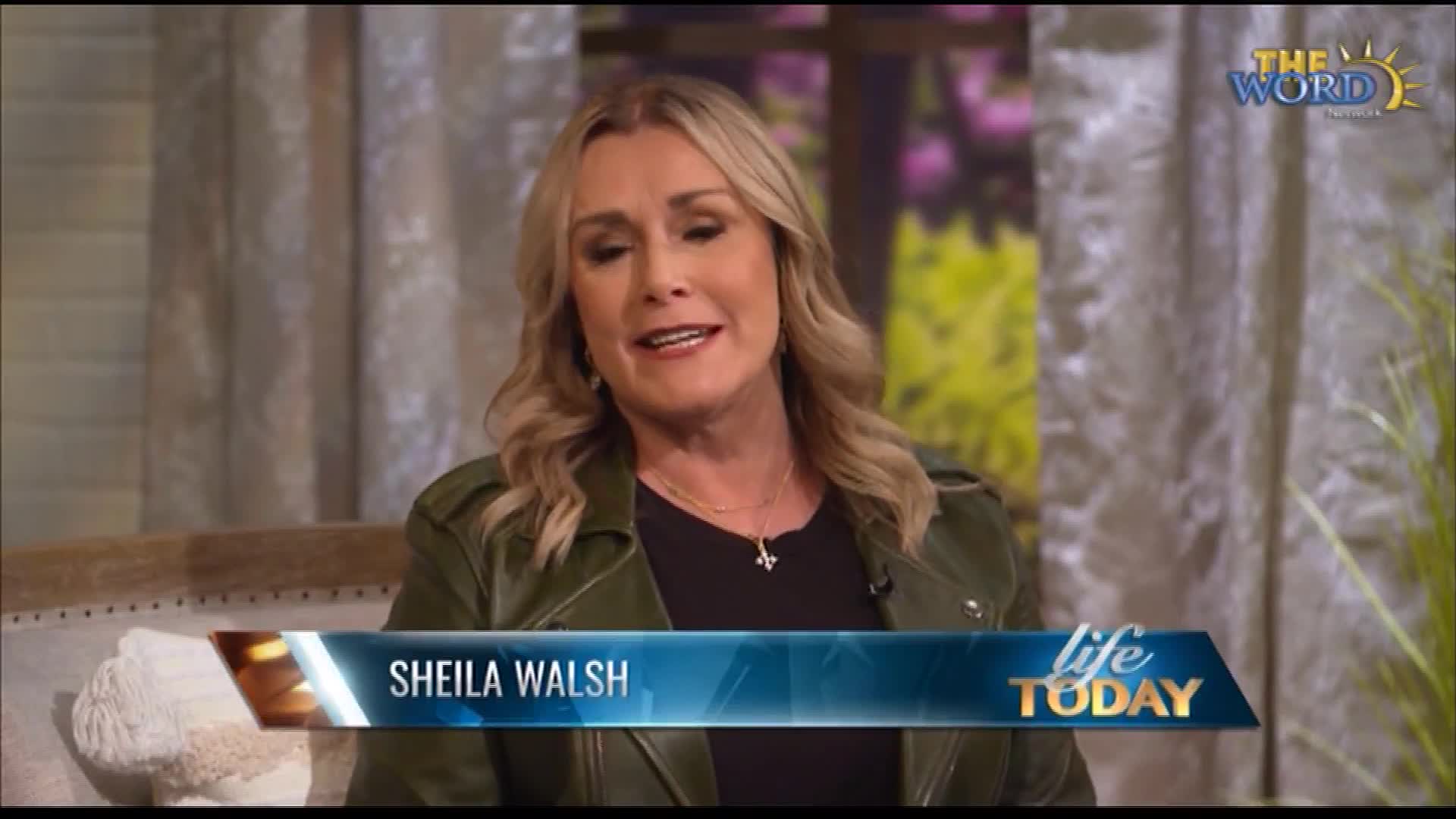 Sheila Walsh is speaking on the set of "Life Today," a show on The Word Network. She's wearing a green jacket and a cross necklace, and she's smiling.
