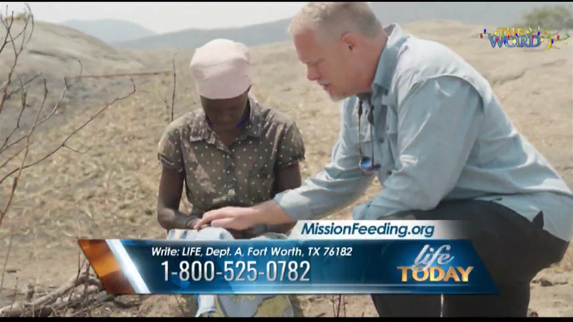 A man in a light blue shirt leans towards a woman wearing a headscarf, both focused on something out of view. The scene is broadcast on "Life Today" from The Word Network, with contact information for MissionFeeding.org at the bottom.
