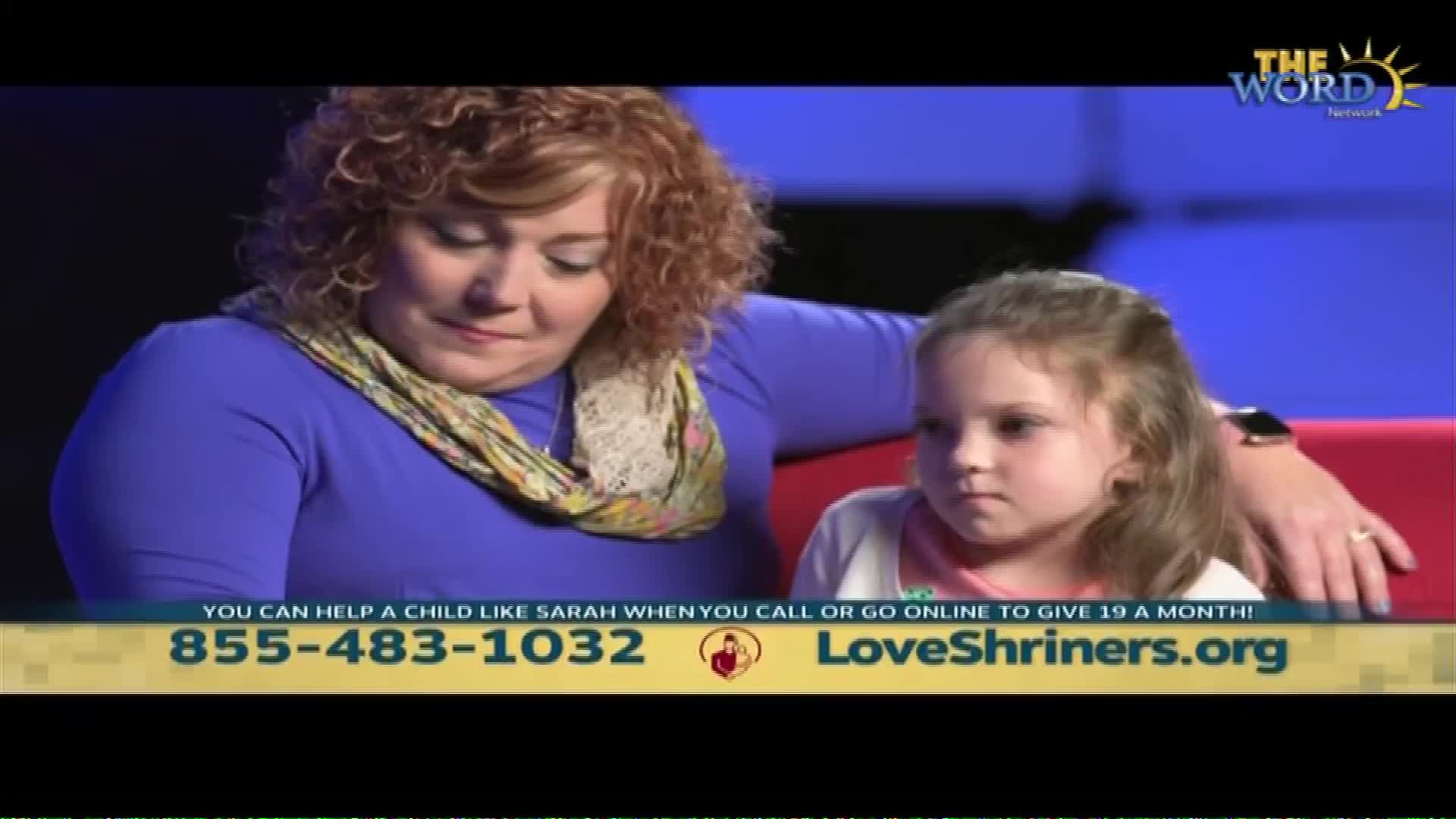 A woman with curly red hair, wearing a purple shirt and a patterned scarf, sits next to a young girl. A logo for The Word Network appears in the upper right corner.