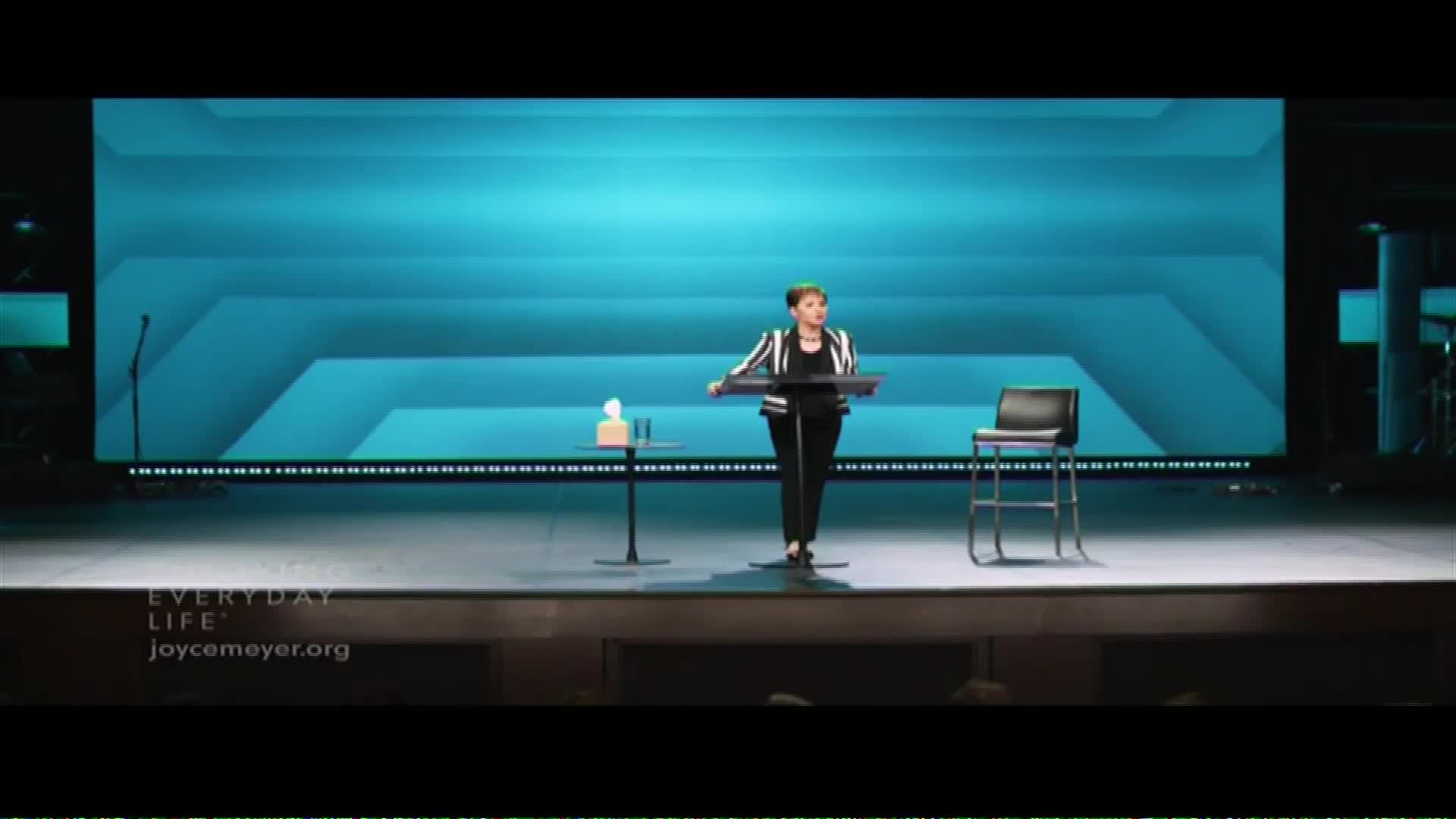 Joyce Meyer stands at a podium on a brightly lit stage, speaking to an unseen audience. The Word Network logo appears at the bottom of the screen.