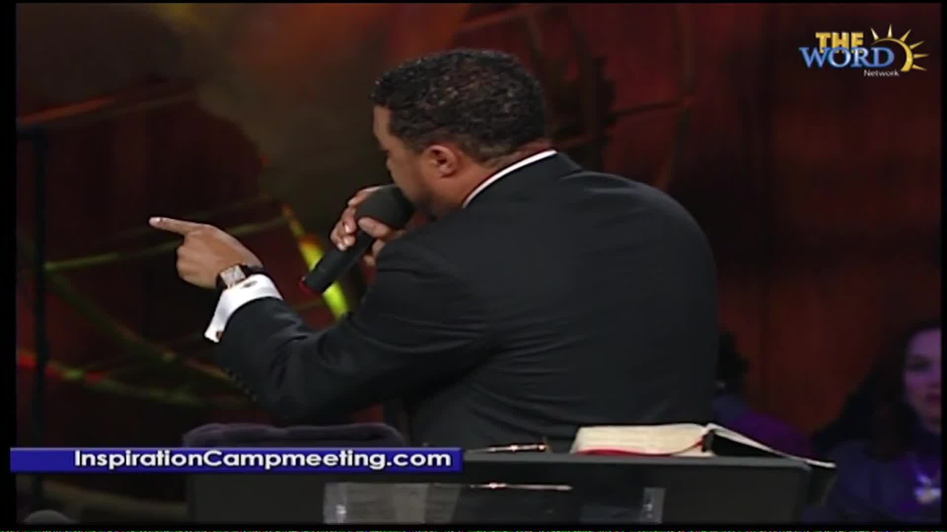 A man in a suit speaks into a microphone, pointing his left hand forward. The Word Network logo appears in the upper right corner, and "InspirationCampmeeting.com" is displayed at the bottom.