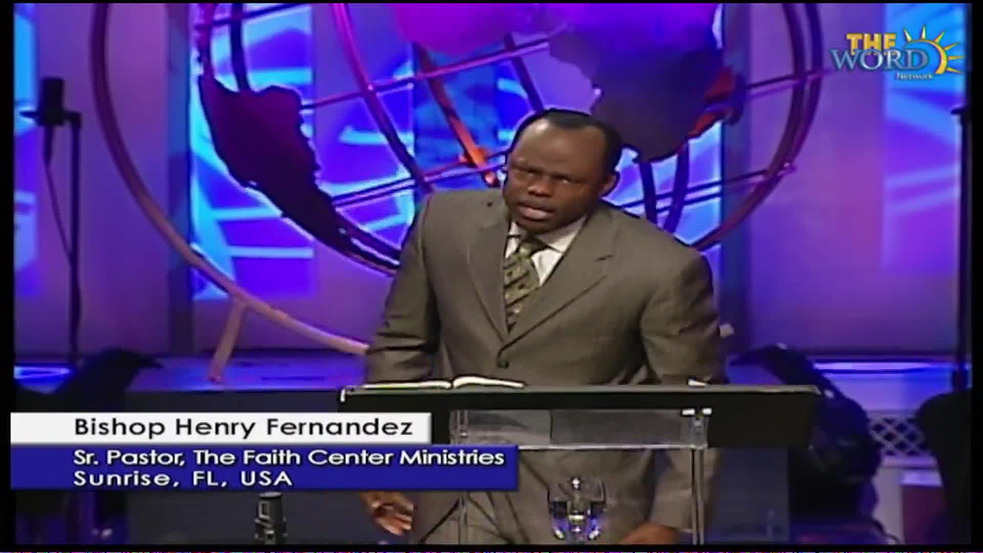 Bishop Henry Fernandez stands at a pulpit in Sunrise, Florida, speaking into a microphone. The Word Network logo is visible behind him.