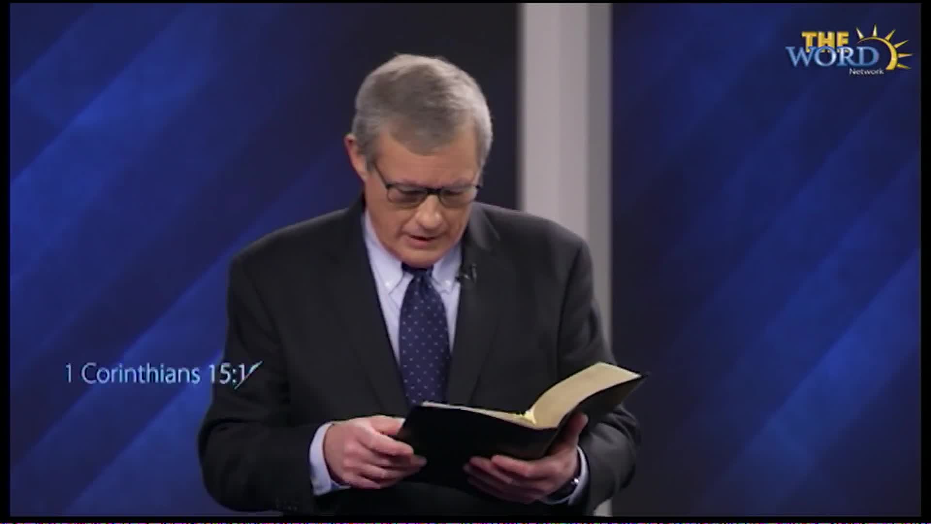 A man in a suit stands before a blue backdrop, reading from a thick book. The Word Network logo is visible in the upper right corner.