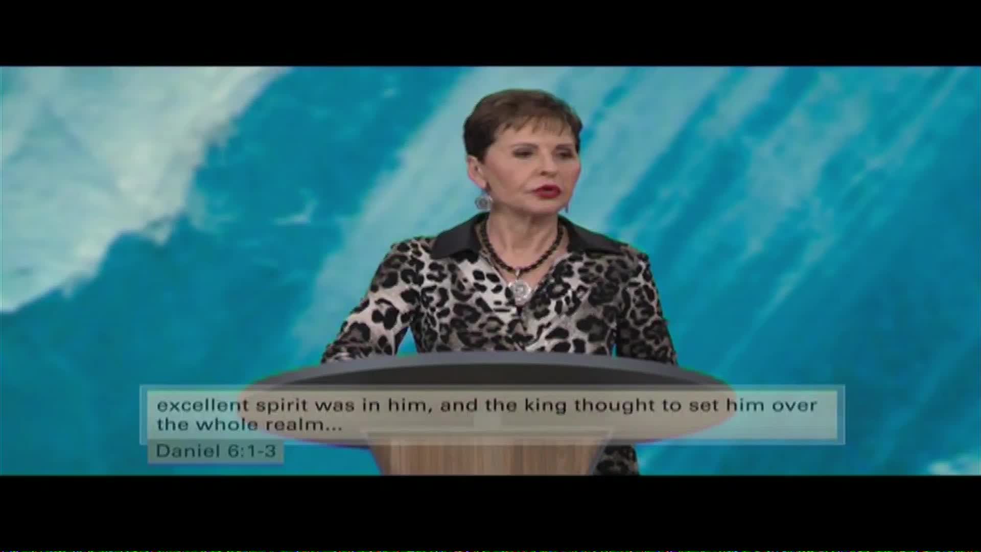 A woman in a leopard-print jacket stands at a podium, speaking. Text on the screen reads, "excellent spirit was in him, and the king thought to set him over the whole realm... Daniel 6:1-3."