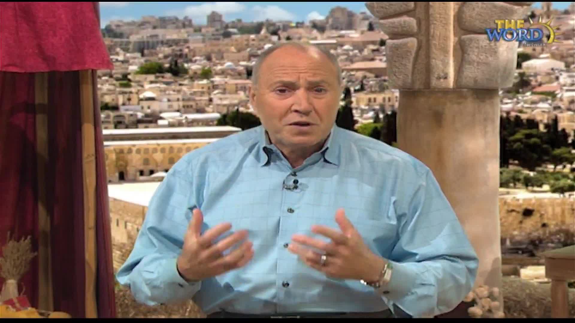 A man in a light blue shirt gestures with both hands as he speaks. Behind him, a cityscape with stone buildings stretches out under a bright sky, with a logo for "The Word Network" visible.