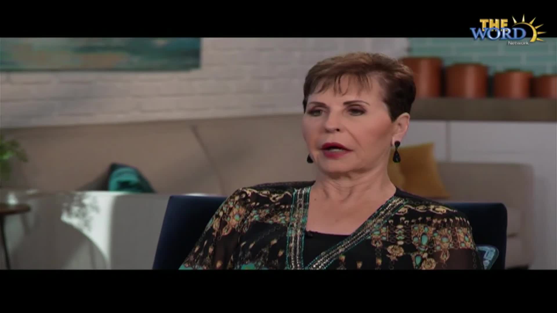 A woman with short brown hair speaks from a chair, her patterned blouse catching the light. The Word Network logo sits in the corner of the screen.
