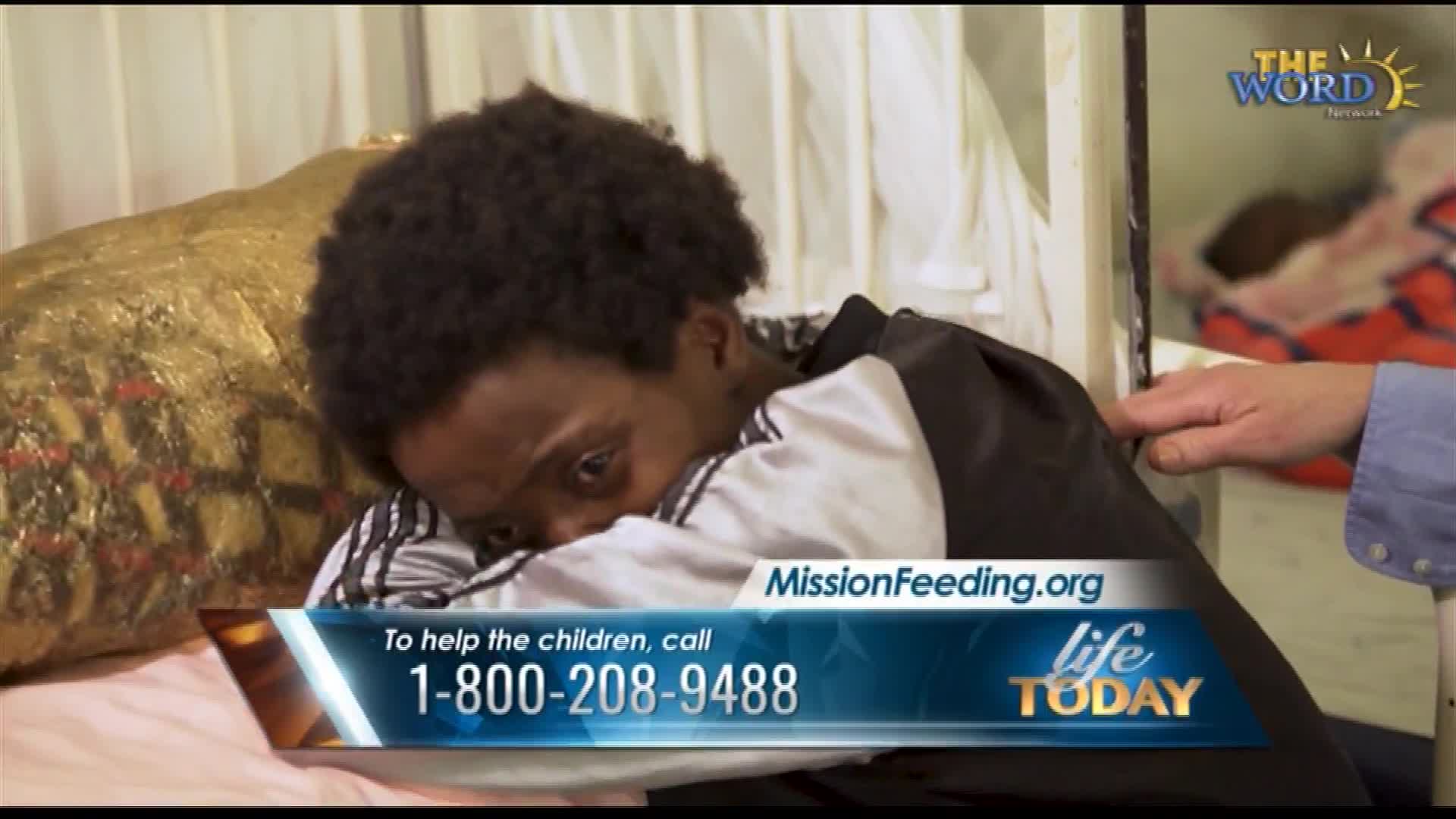 A young person curls up on a bed, head buried in their arms. A hand rests gently on their shoulder, offering comfort.