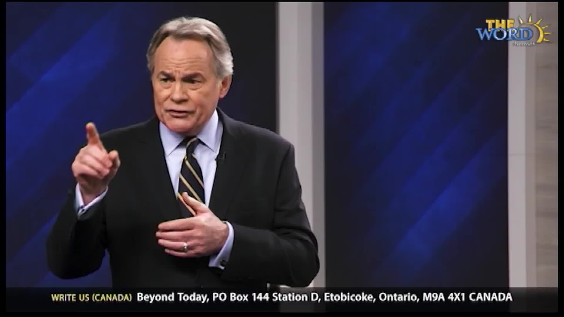 A man in a suit and tie gestures with his right hand, pointing his index finger forward. He speaks with conviction, his left hand resting on his chest.