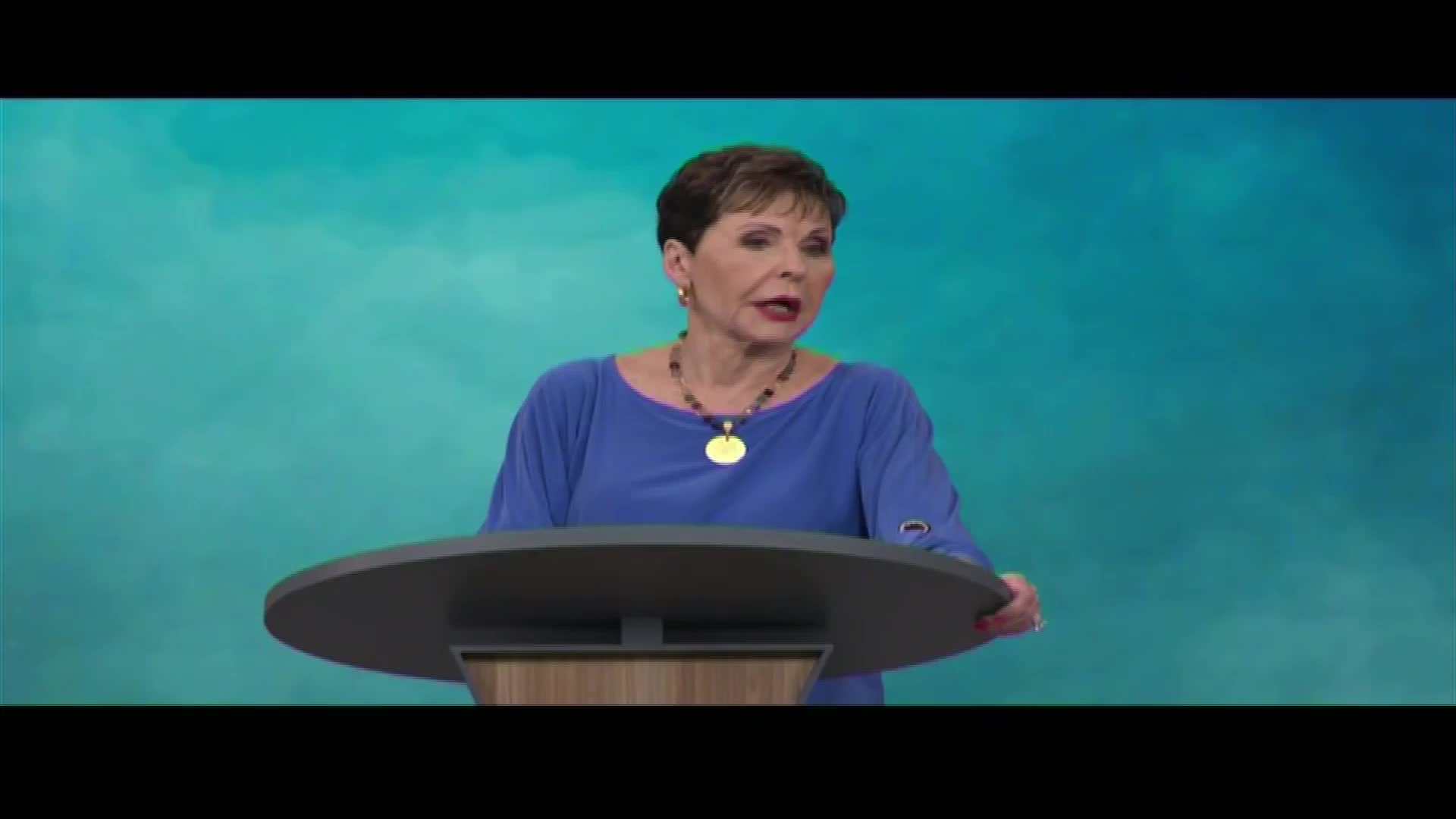 A woman in a blue shirt stands behind a podium, speaking. Her message is broadcast across the United States on The Word Network.