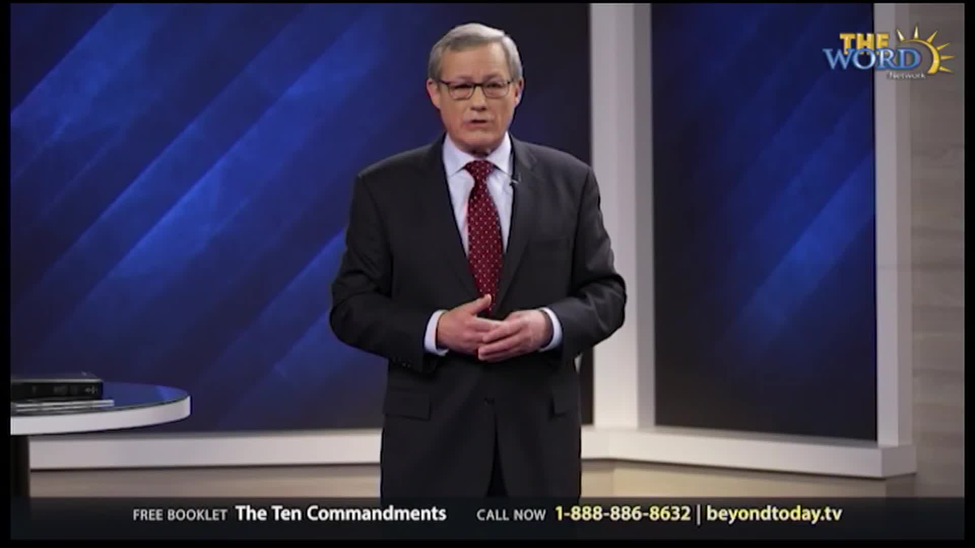 A man in a dark suit stands on a stage, speaking. The Word Network logo is visible in the upper right corner.