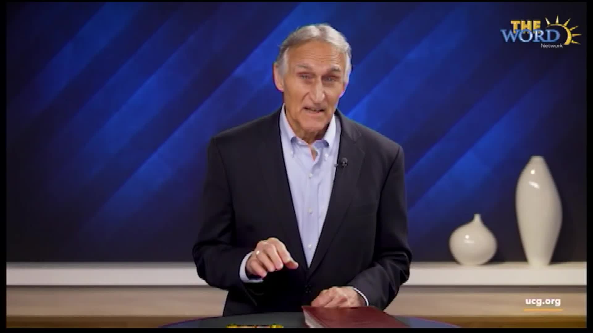 A man in a suit stands behind a lectern, gesturing with his right hand while speaking. The Word Network logo appears in the upper right corner of the screen.