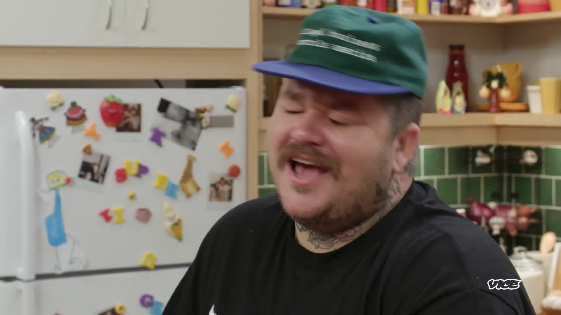 The man in a green and blue cap is talking, his mouth wide open. He's in a kitchen, and the VICE TV logo is in the corner.
