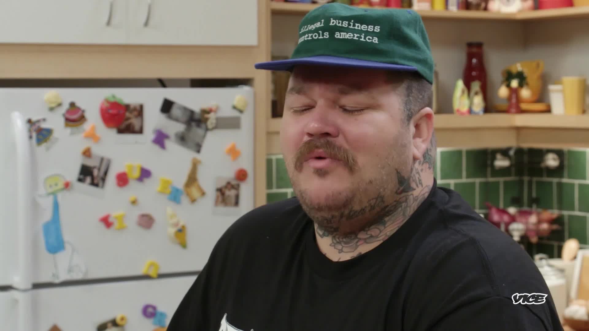 A man with a mustache and tattoos wears a green hat, eyes closed, and his mouth slightly open. The VICE logo is visible in the corner of the frame.
