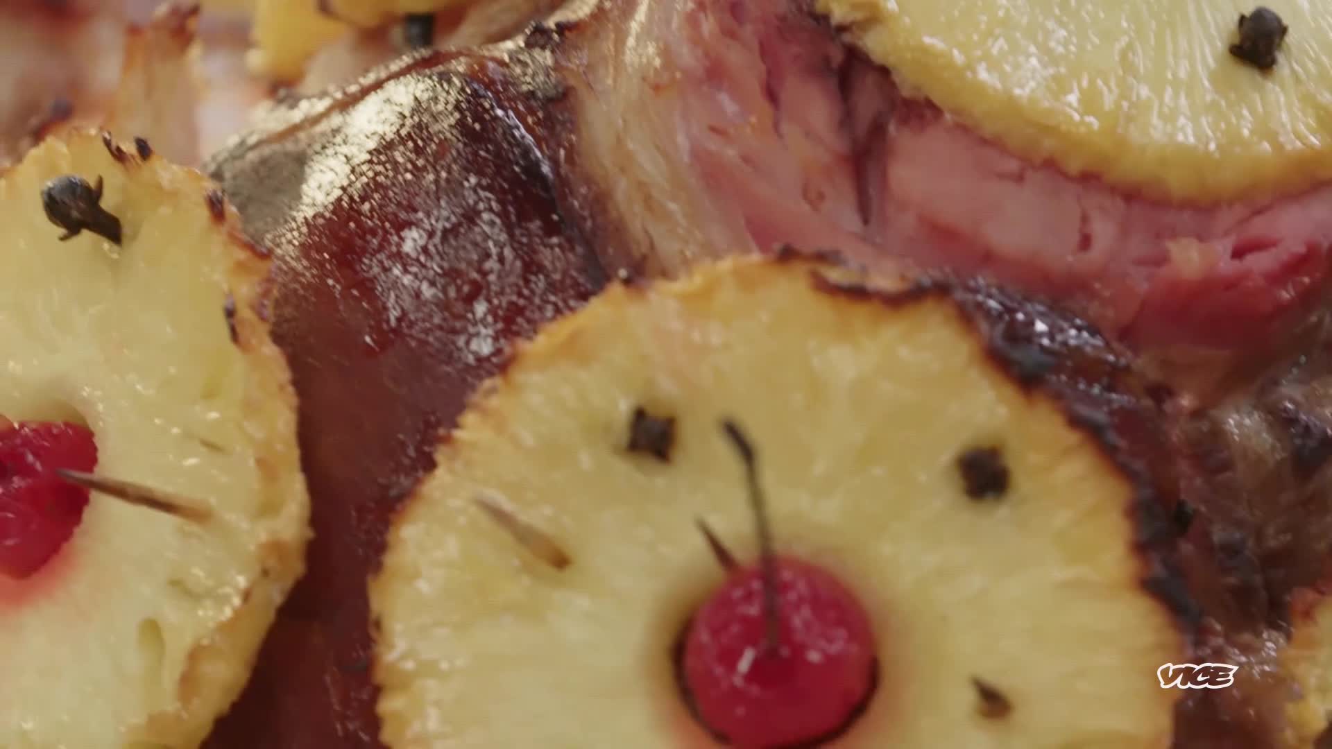 A glazed ham, studded with cloves, is decorated with pineapple slices. Each slice has a cherry and toothpick, as seen on VICE TV.
