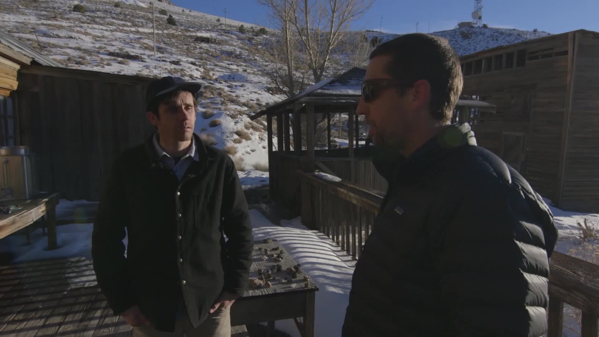 Two men stand on a wooden deck, framed by a snowy landscape. The VICE TV crew is filming outside, with a backdrop of a faded wooden structure and a snow-covered hill.
