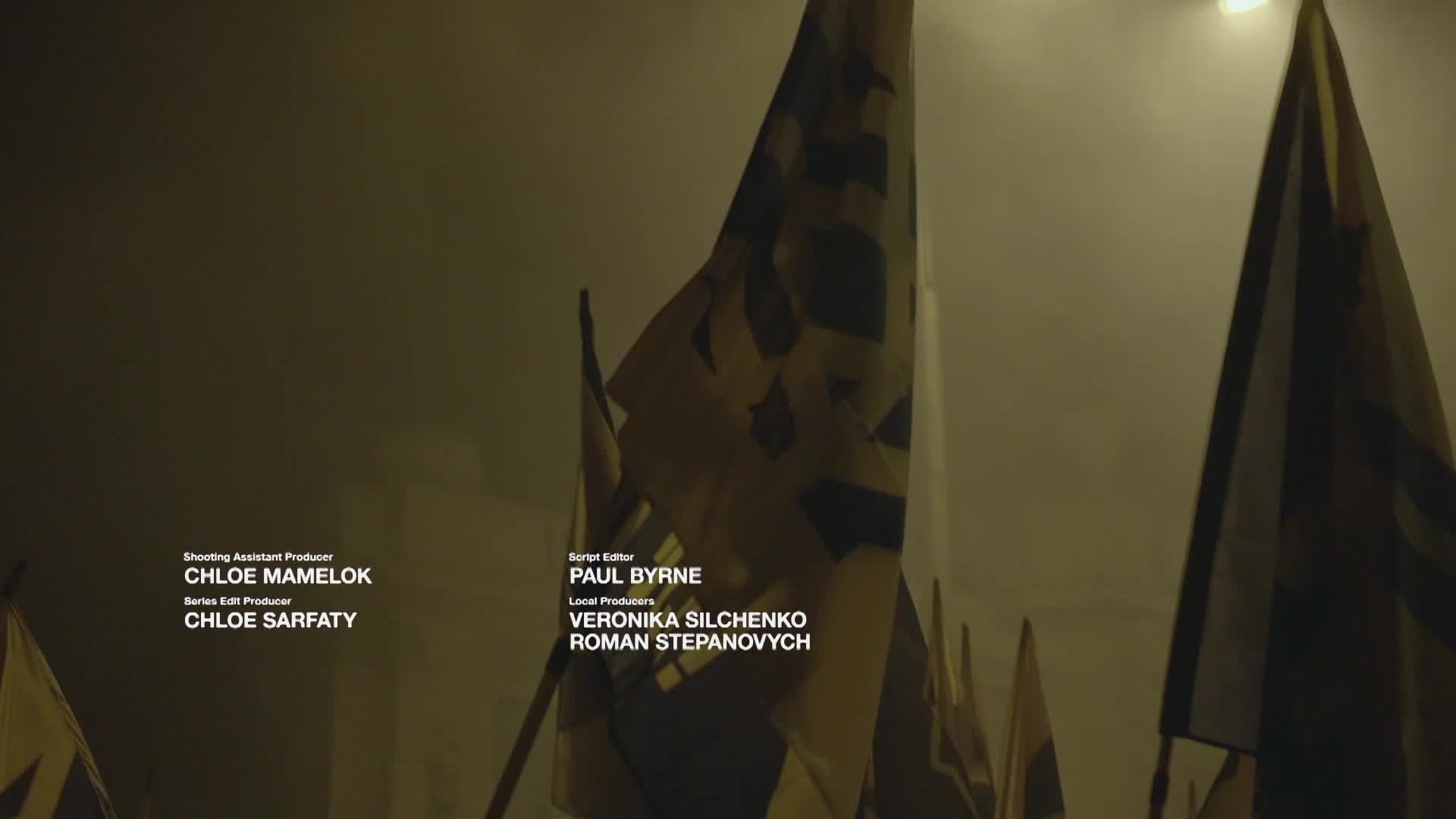 Flags with black and yellow designs fill the frame, partially obscuring the credits for a VICE TV production. The flags sway gently, lit by a single overhead light.
