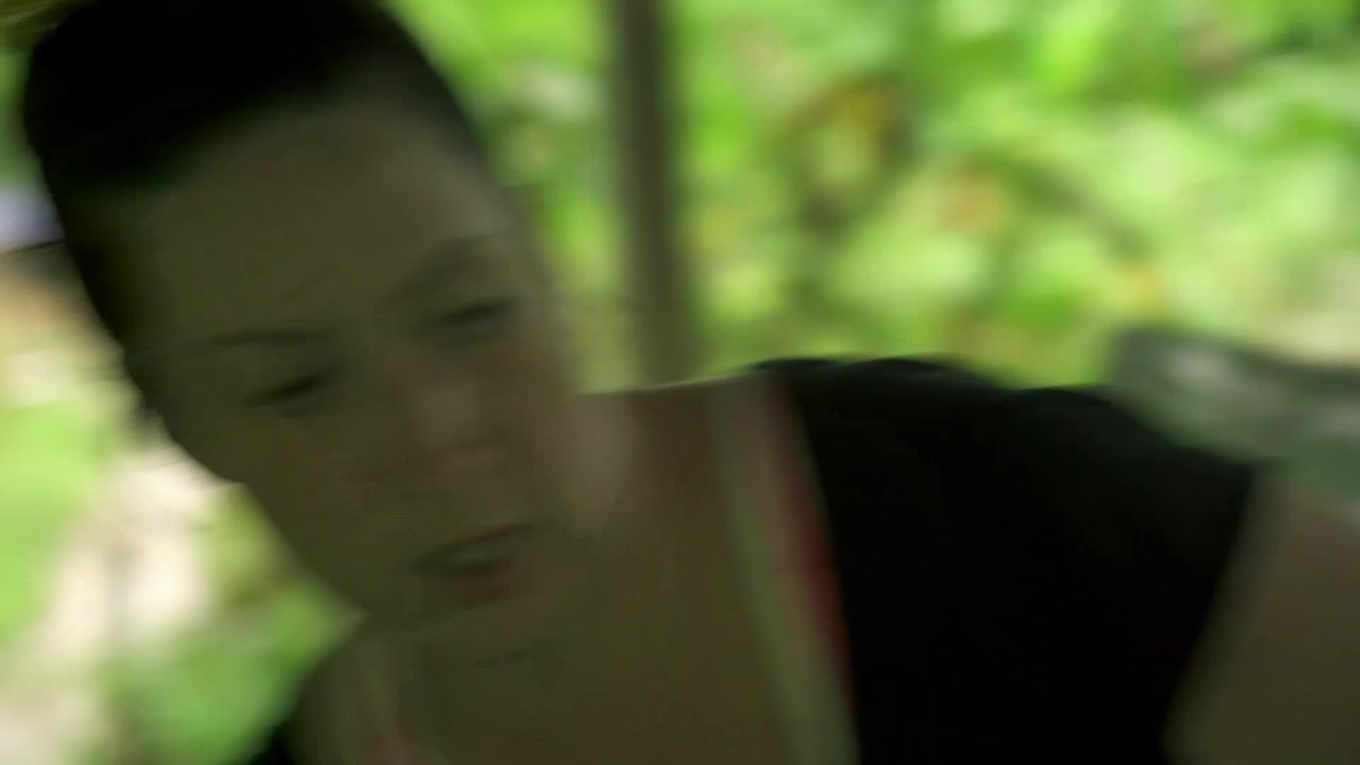 A woman with a shaved head is looking down, her face partially obscured by the motion. The background is a wash of green, suggesting a forest setting.
