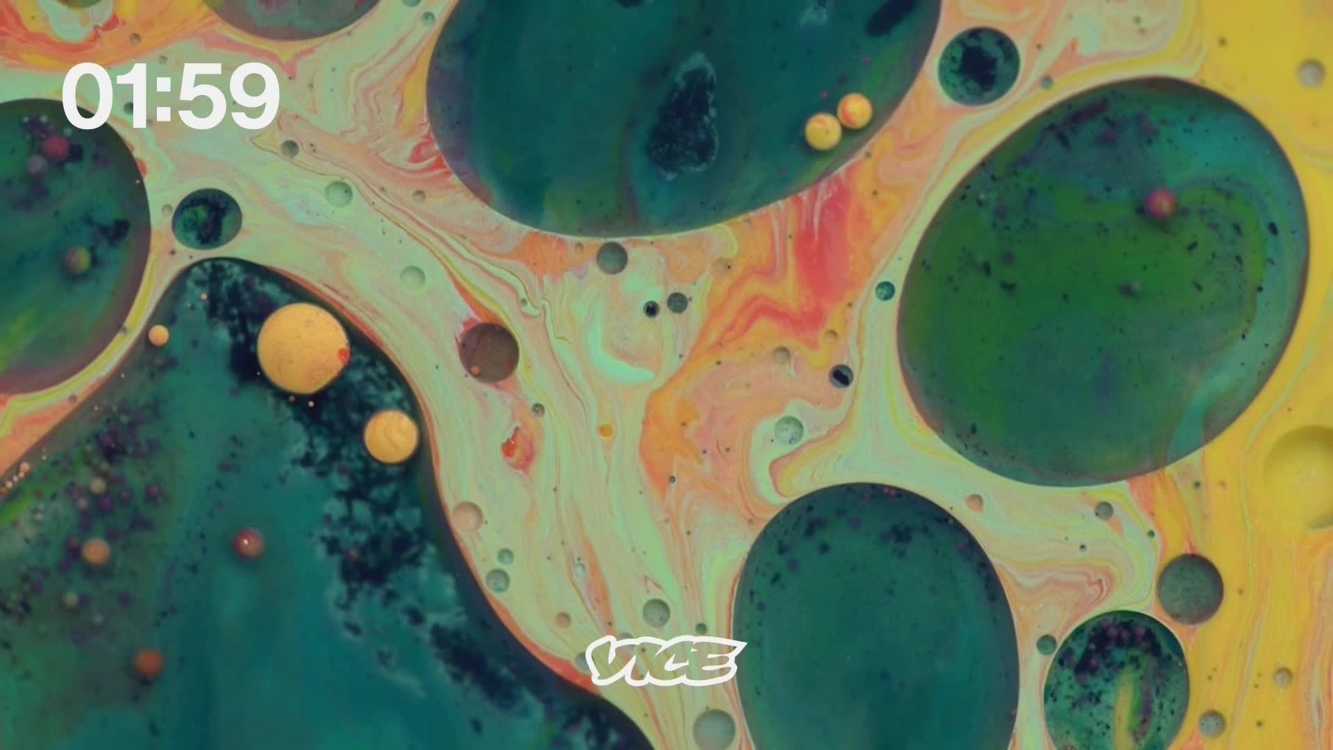 The clock reads 01:59 as vibrant green and yellow liquids swirl together. Tiny orange spheres drift through the colorful currents, a signature VICE logo peeking out from the bottom.
