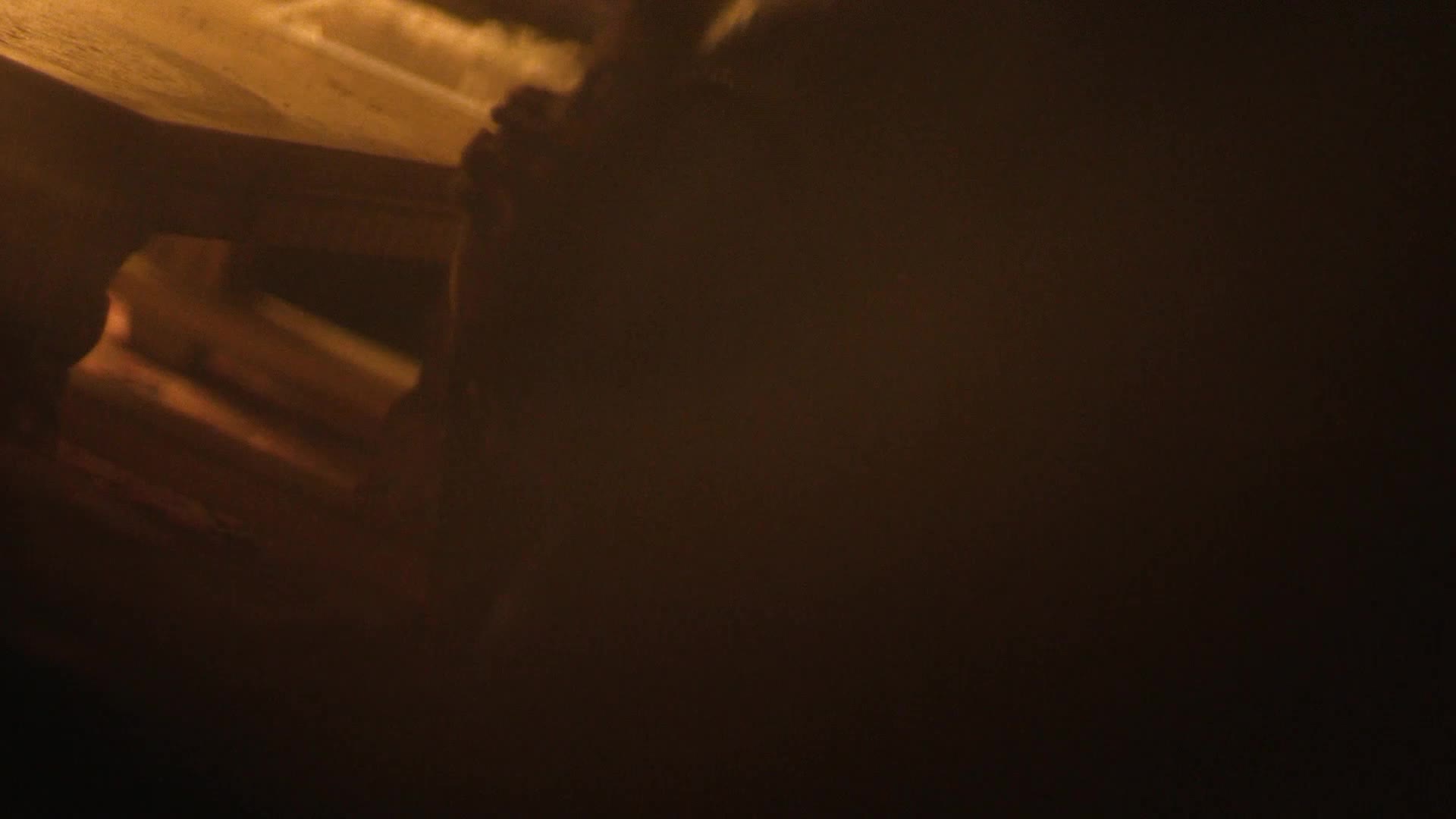 A figure in the foreground, likely a man, is leaning over a wooden surface, his hands obscured by shadow. The scene is bathed in a warm, hazy glow, suggesting an indoor setting, perhaps a workshop or a dimly lit room.