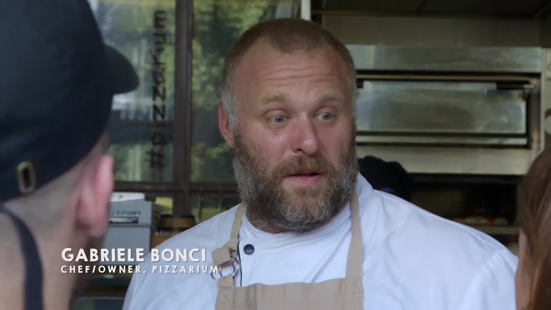 Gabriele Bonci, chef and owner of Pizzarium, speaks animatedly, his beard catching the light. Behind him, a pizza oven glows, ready for the next pie.