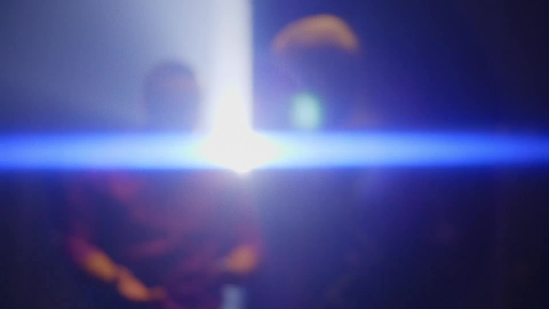 A bright white light beams down, catching the shoulders of two figures in the darkness. A sharp blue line cuts across the frame, obscuring the details of the scene.