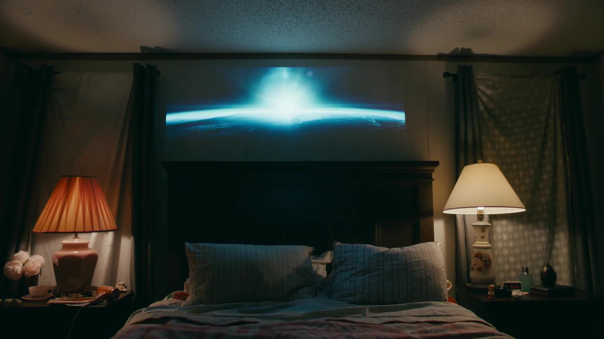A bright, blue light emanates from a projection on the wall above a bed. The scene feels like a quiet moment at home, perhaps after a long day of filming for VICE.