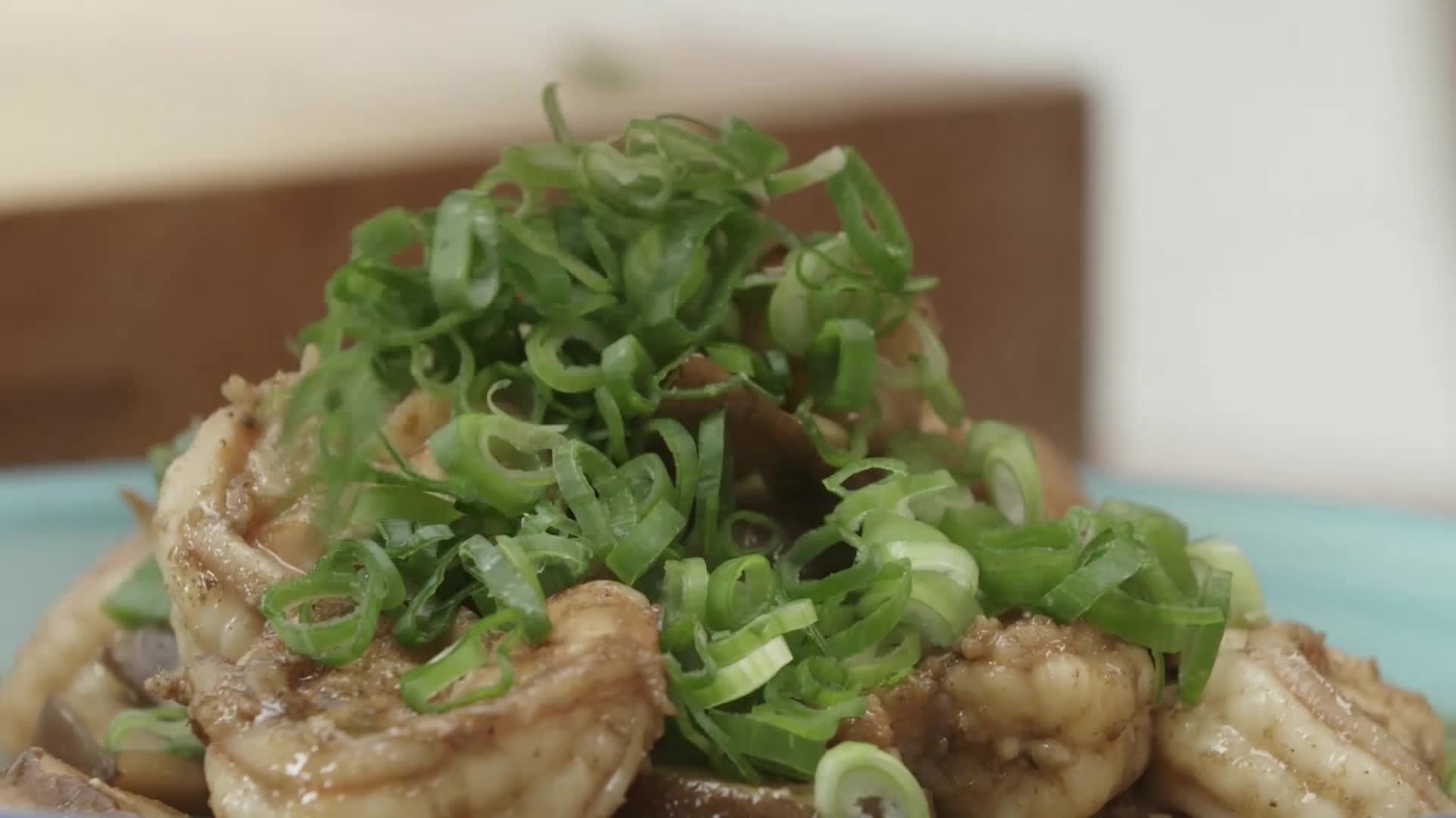 A pile of glistening shrimp, coated in a savory sauce, is generously topped with bright green scallions. This dish, likely featured on a VICE TV segment about American food culture, looks ready to be served.