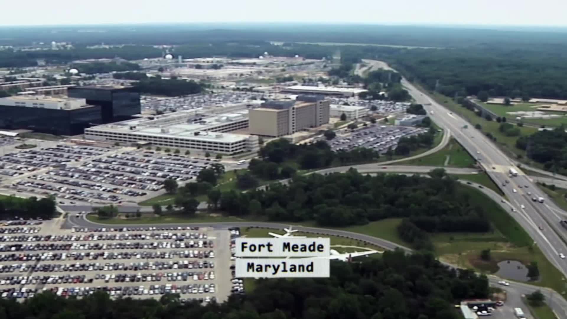 Cars fill vast parking lots outside imposing, modern buildings. A highway snakes through the landscape, carrying trucks and cars toward the horizon.