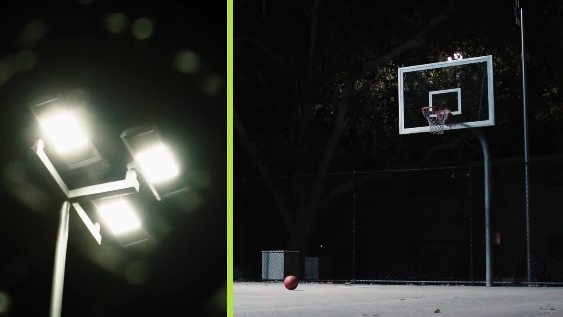Bright stadium lights cut through the darkness, illuminating an empty basketball court. A lone red basketball sits on the asphalt, waiting for a game.