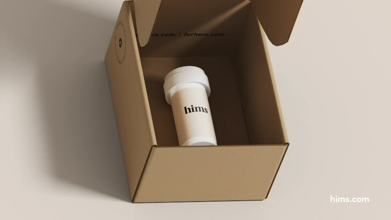 Inside an open cardboard box, a prescription bottle labeled "hims" sits upright. The box is plain, with a simple design and a website address printed on the inside flap.
