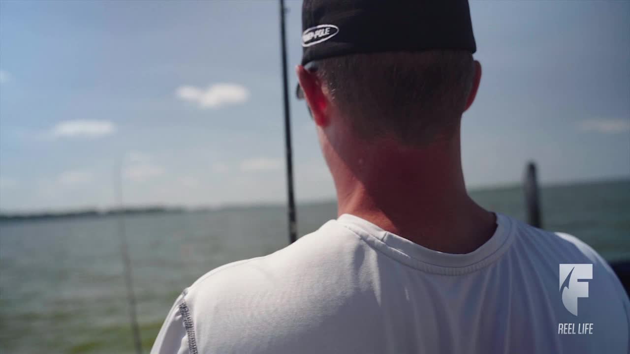 The man, wearing a cap, stares out at the water. He's on a boat, with fishing rods visible, and the World Fishing Network logo is in the corner.
