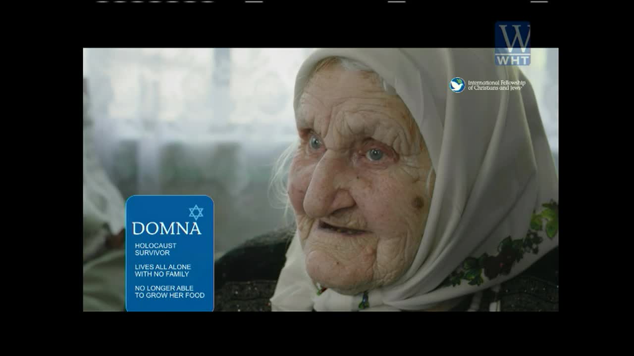 An elderly woman, wearing a headscarf, looks directly at the camera. A blue graphic on screen, likely from World Harvest TV, identifies her as a Holocaust survivor.
