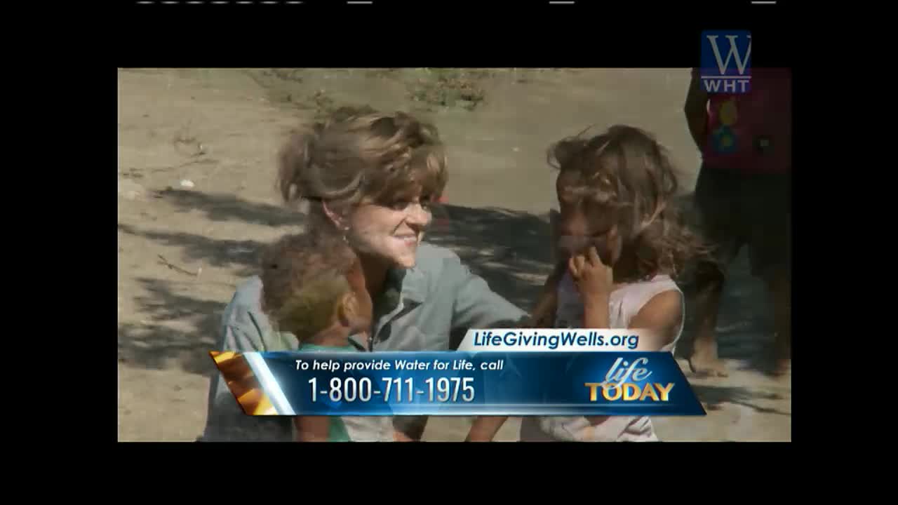 A woman smiles, her arm around a child, while another child stands close by. The scene is part of a "Life Today" segment on World Harvest TV, promoting water for life.
