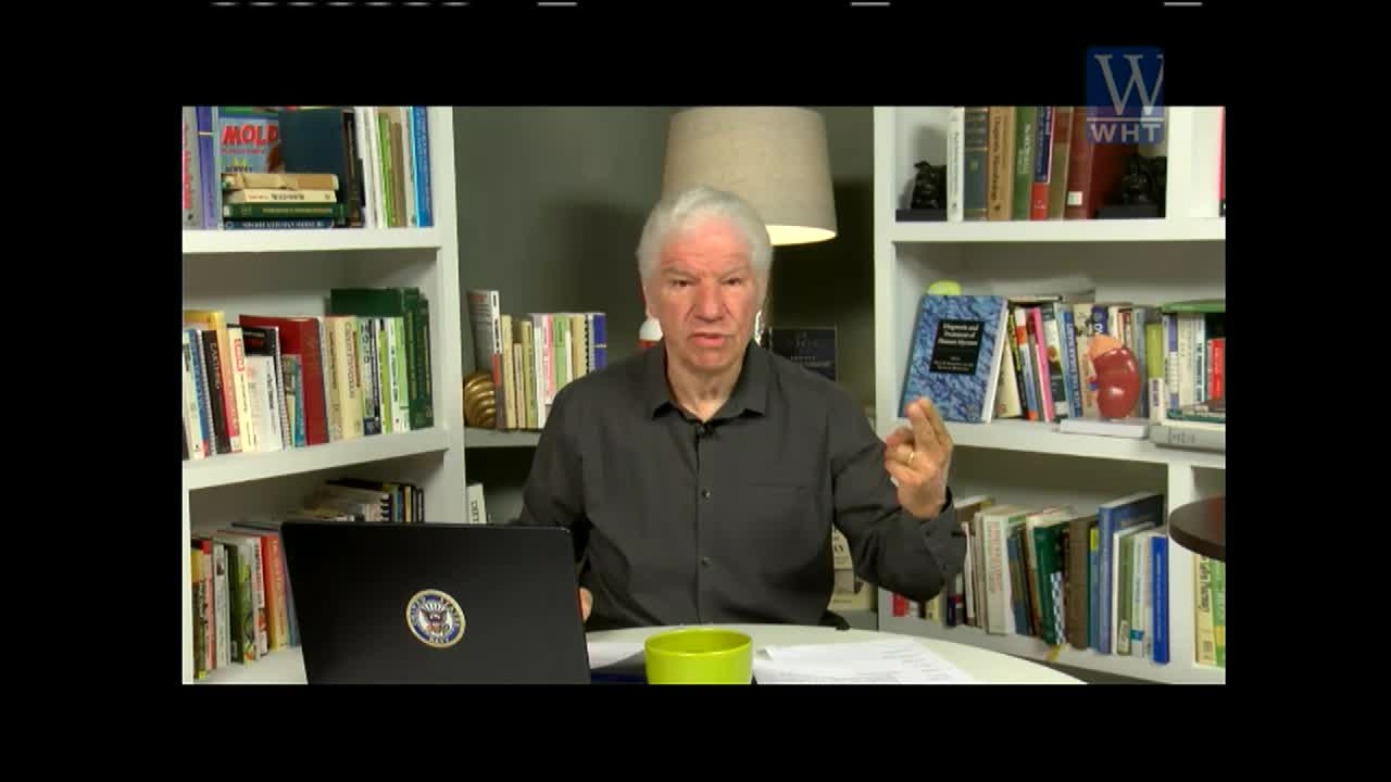 A man with white hair gestures with his hands while speaking, likely on World Harvest TV. He's seated at a desk with a laptop, a green cup, and bookshelves filled with books behind him.
