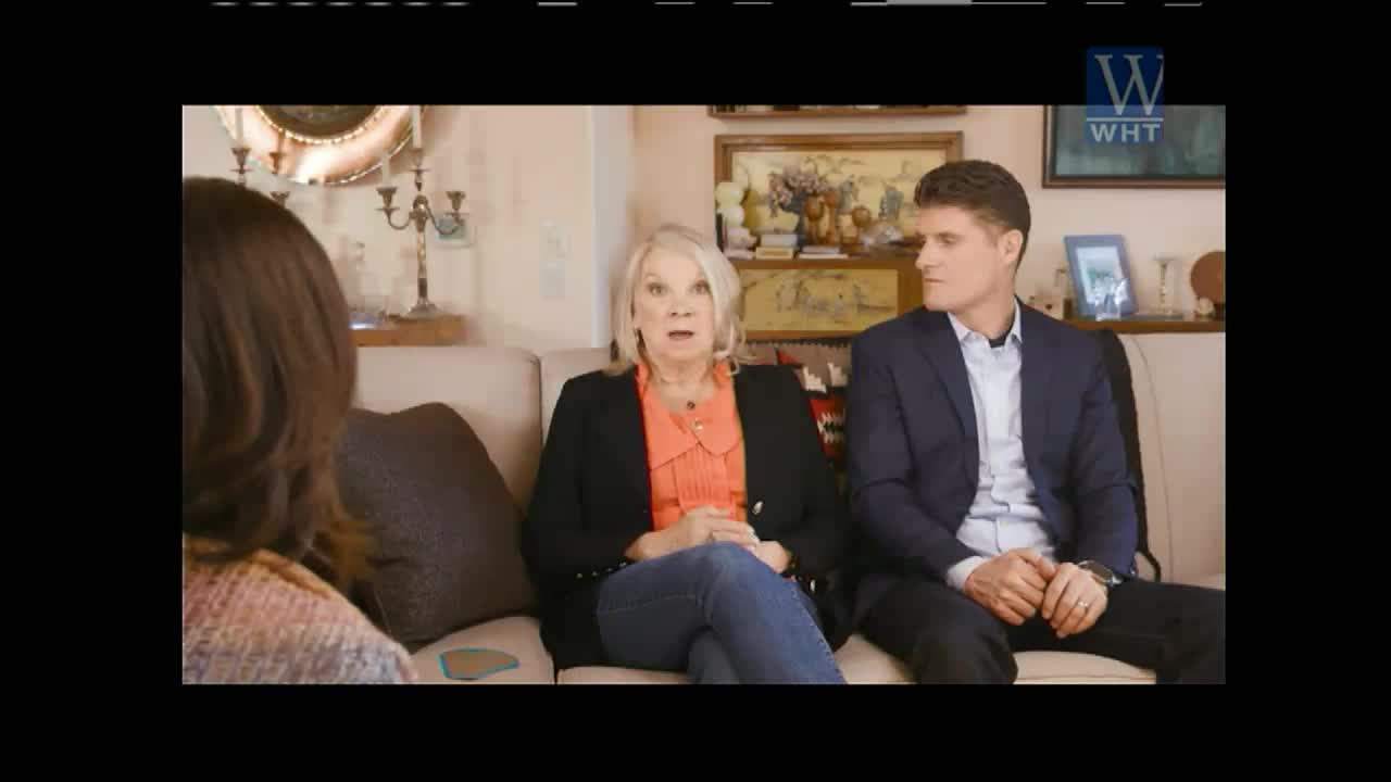 On a set for World Harvest TV, a woman with blonde hair opens her mouth wide, seemingly surprised, while a man in a suit looks to his left. The person interviewing them is out of frame.
