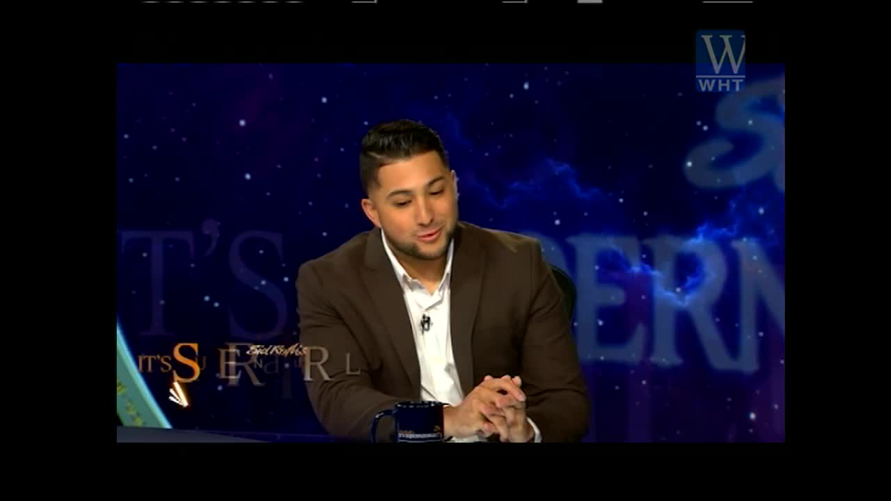 A man in a brown suit sits at a desk, speaking on a set for World Harvest TV. The background is a dark blue with a starry design and the words "It's Supernatural."
