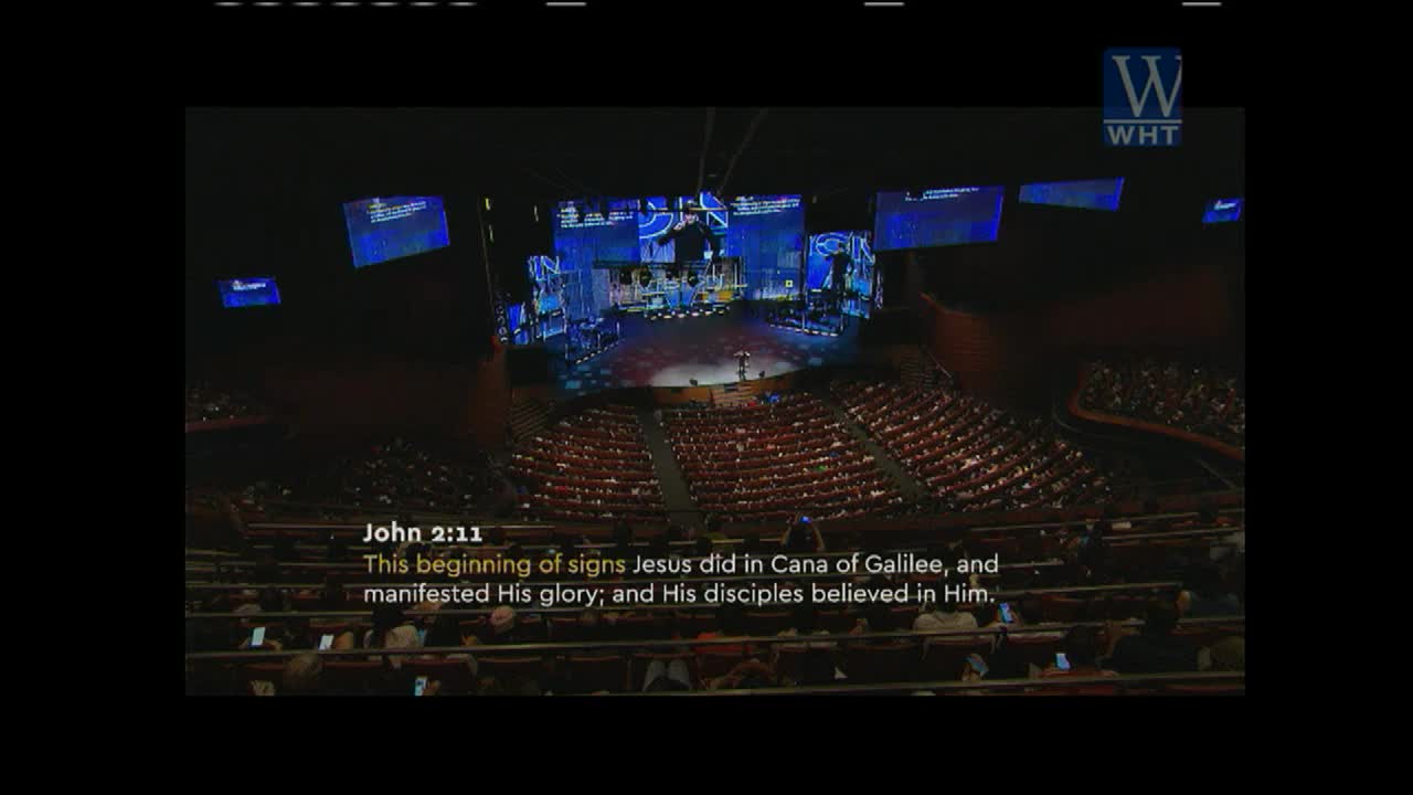 A preacher stands on a large stage, illuminated by bright lights, addressing a packed auditorium. The scene is being broadcast on World Harvest TV, with the text of John 2:11 displayed on the screen.
