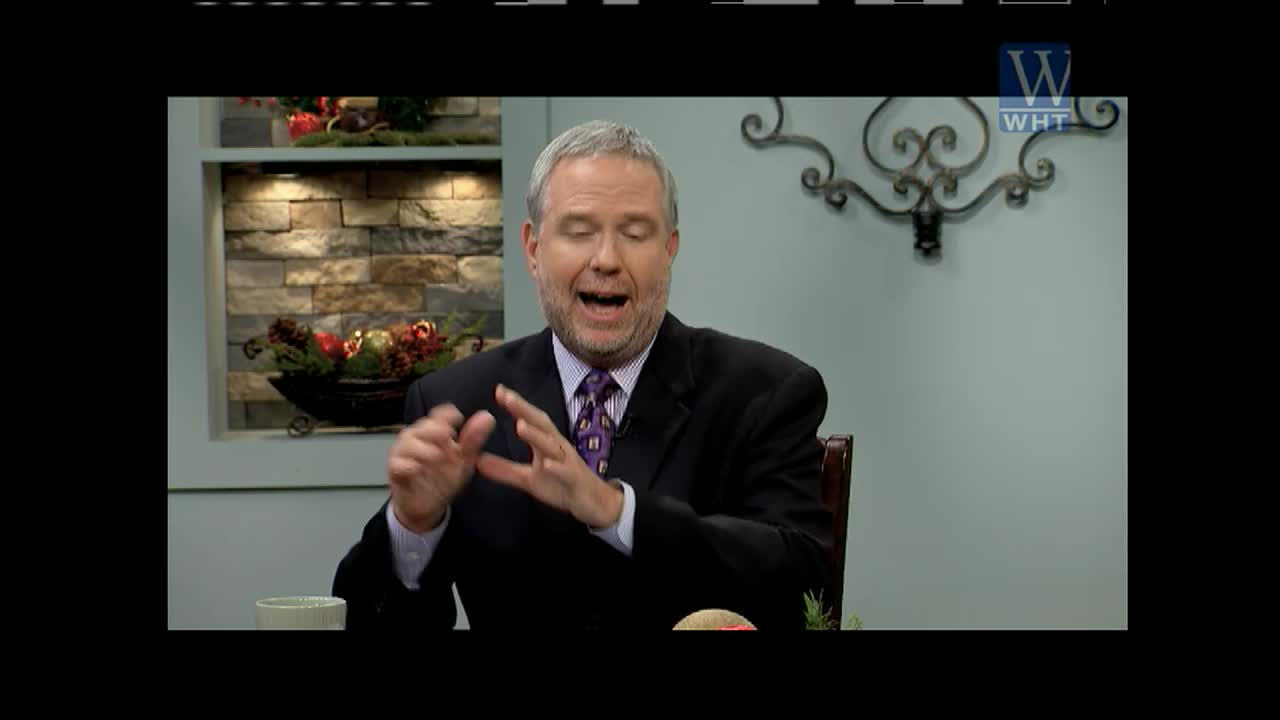 The man in the suit gestures with his hands, speaking passionately. He's on the set of World Harvest Television, in front of a decorative wall.
