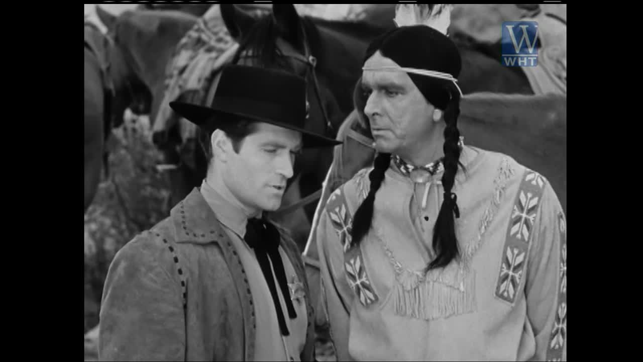 A man in a cowboy hat and a man in Native American attire stand close, deep in conversation. Horses are visible behind them, suggesting a scene from a Western film broadcast on World Harvest TV.