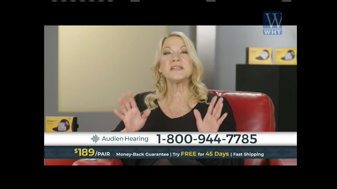 A woman with blonde hair gestures with both hands as she speaks, seated in a red chair. A graphic at the bottom displays "Audien Hearing" and a phone number.
