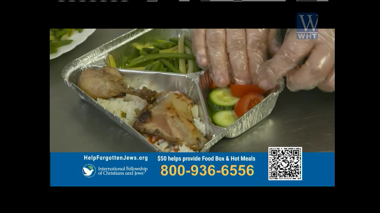 Gloves are carefully placing sliced tomatoes and cucumbers into a compartmentalized foil tray. This tray already holds rice with chicken pieces and a side of green beans.