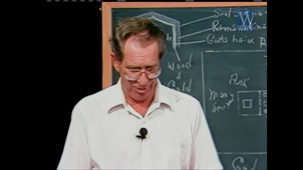 A man in a white shirt stands before a chalkboard with diagrams and writing. He looks down, his glasses perched on his nose.