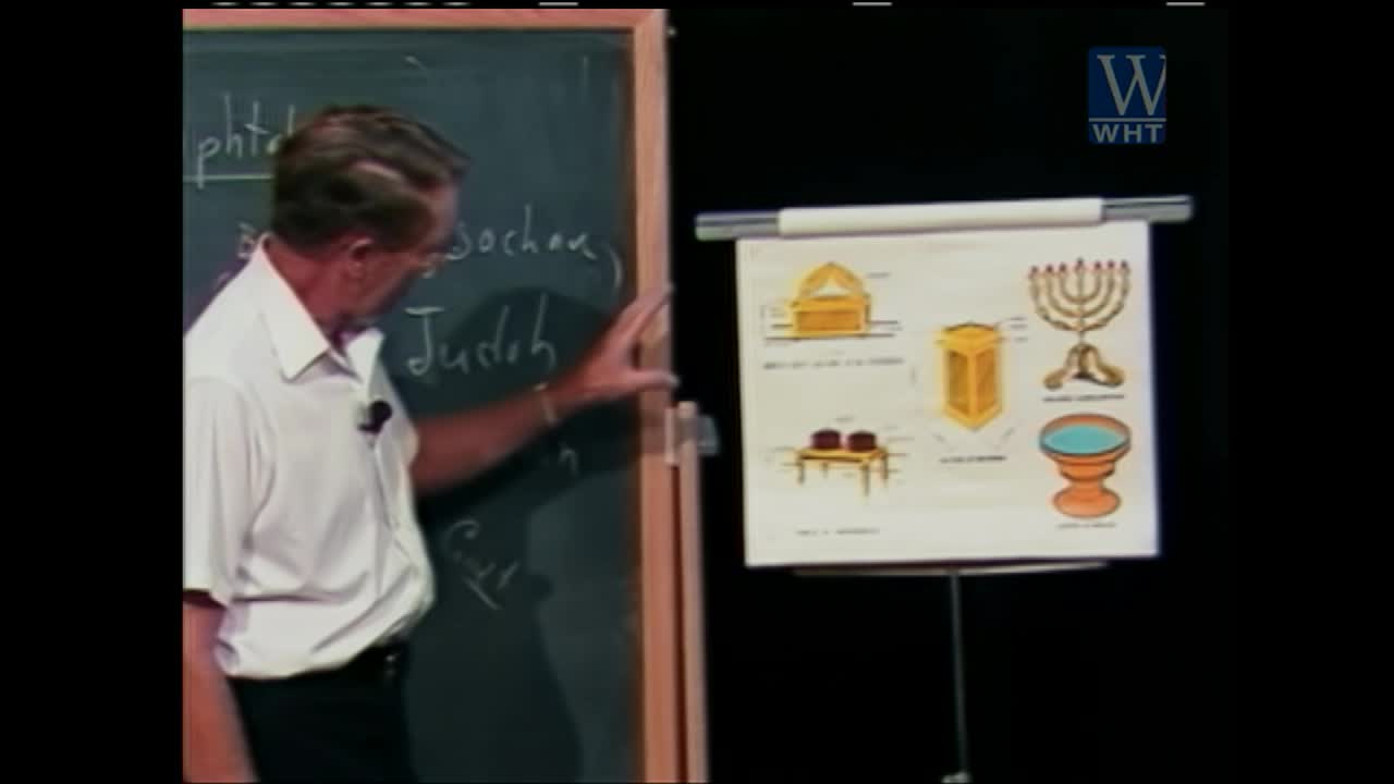 A man in a white shirt gestures towards a chalkboard with handwritten notes, while a chart displaying religious symbols hangs on an easel beside him. The World Harvest Television logo is visible in the upper right corner.