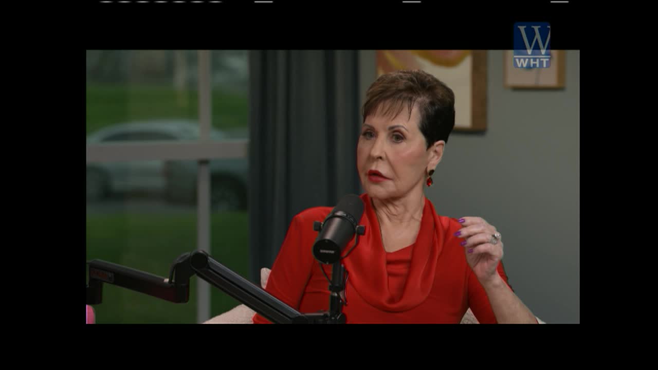 A woman in a red top speaks into a microphone, her hand gesturing slightly. Outside the window, a car is visible, its details blurred by the glass.
