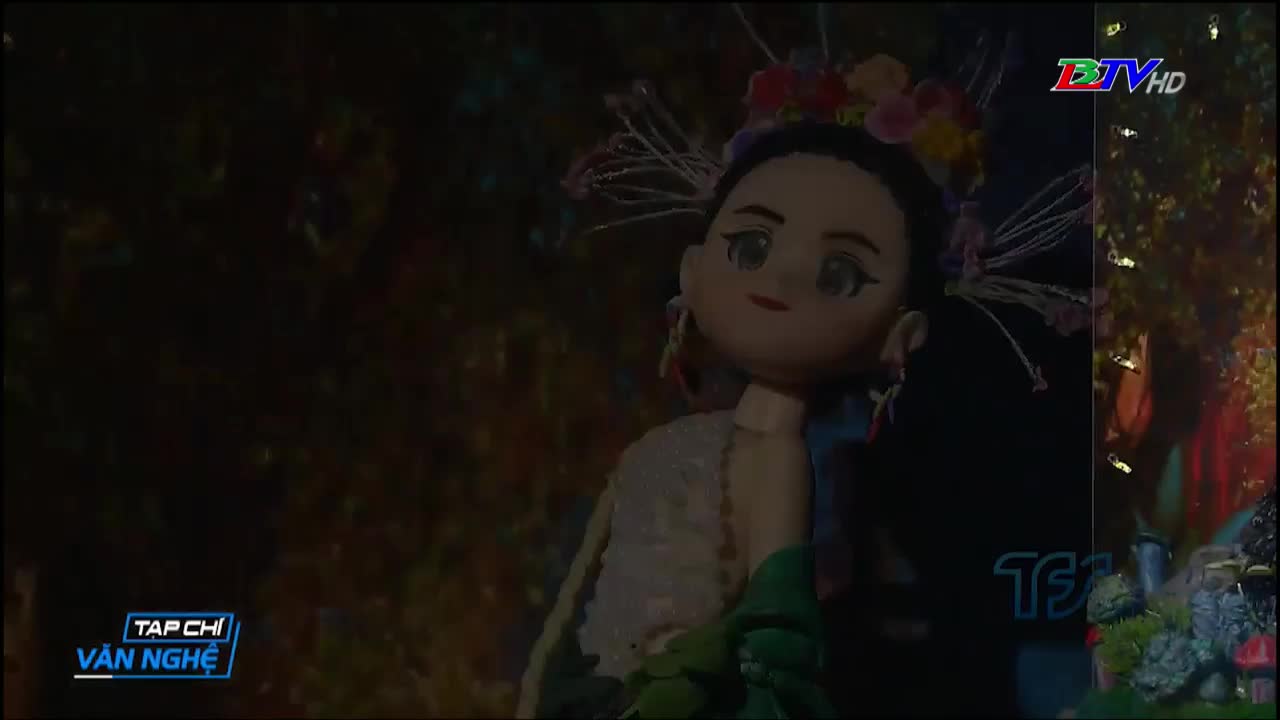 A large puppet, adorned with flowers, is front and center, its painted face gazing out. The scene is likely part of a performance, possibly broadcast by Bac Lieu TV, with the "Tap Chi Van Nghe" logo visible.
