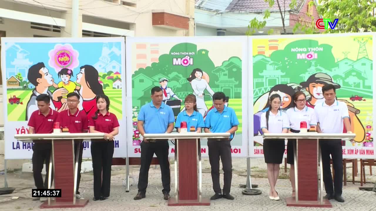 Three teams stand behind podiums, each with a red buzzer, facing a backdrop of colorful posters. The scene looks like a game show, possibly related to "New Rural Areas" in Vietnam, as the Bac Lieu TV logo is visible.

