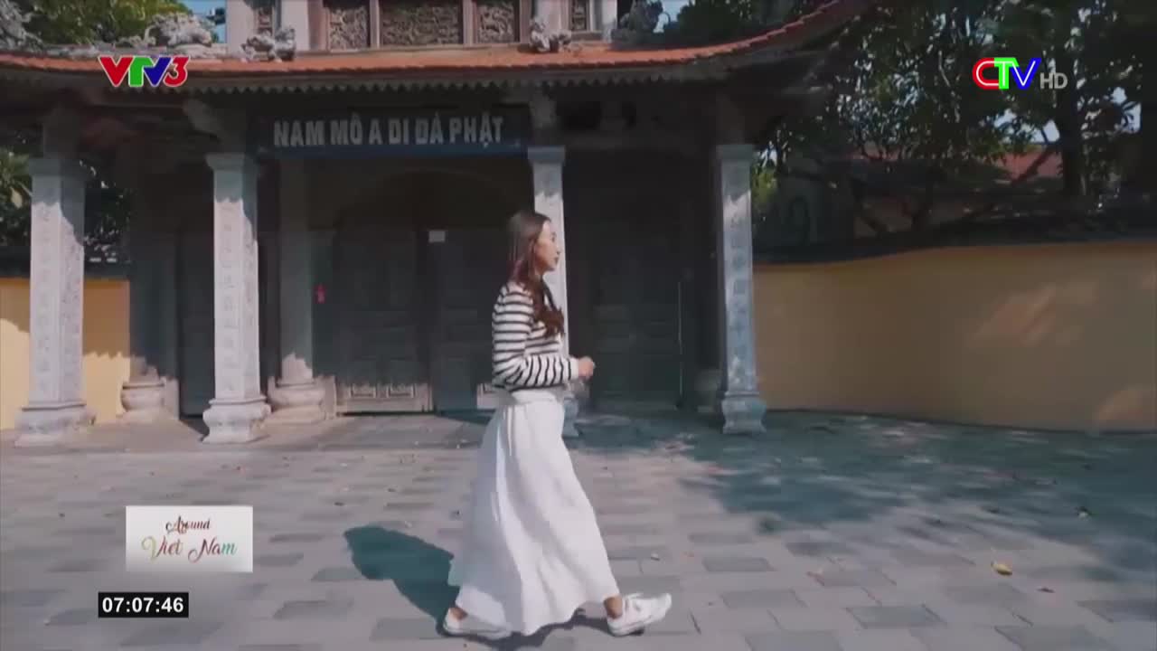 A woman in a striped shirt and a flowing white skirt strides past a temple entrance. The scene is framed by the logos of Vietnamese TV stations, suggesting a broadcast from Bac Lieu.
