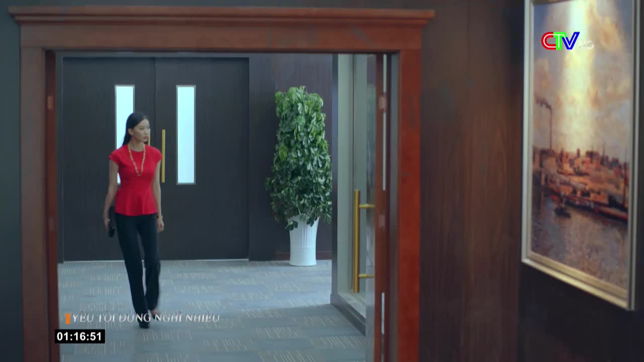 A woman in a red top strides toward the camera, holding a small black clutch. The scene is from a Vietnamese TV show, and the timecode reads 01:16:51.

