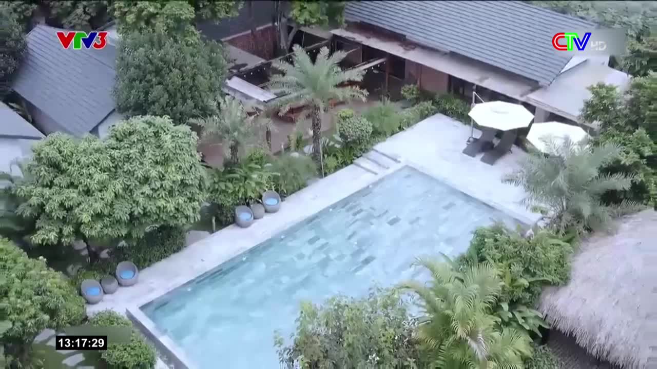 A rectangular pool shimmers in the sunlight, surrounded by lush greenery and a thatched roof structure. The scene is broadcast on Vietnam TV, with the time displayed in the corner.
