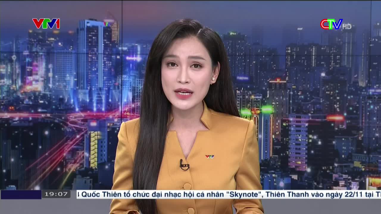 A woman in a gold blazer speaks directly to the camera, against a backdrop of a city skyline at night. The VTV logo is visible on the screen, and text at the bottom mentions a music festival.
